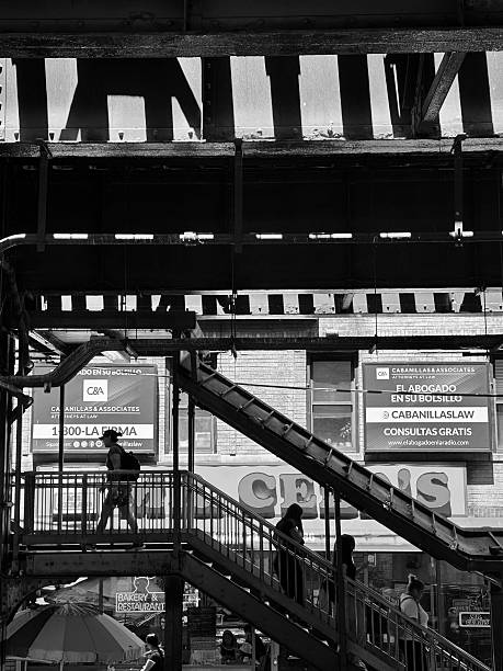 New York, New York, USA- June 24, 2025: People move up and down a diagonal stairwell under the elevated 7 train along Roosevelt Avenue in Corona, Queens.