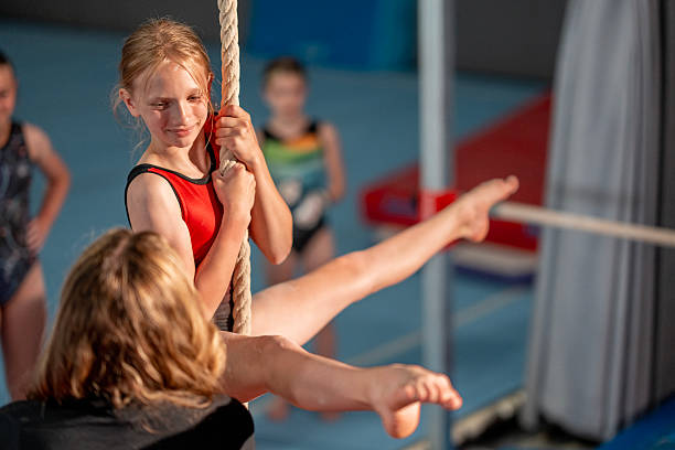 A group of young gymnasts practicing on various equipment under professional supervision in a gym. The scene shows teamwork, focus, and athletic development, reflecting determination and the joy of learning skills.
