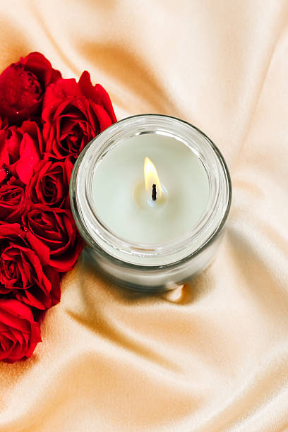 istock Elegant candle surrounded by red roses on silky fabric in a romantic setting 2223262215