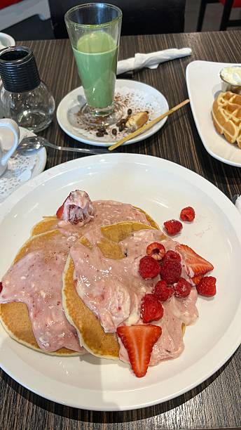 A delicious breakfast scene showcasing fluffy pancakes topped with fresh strawberries and raspberries, complemented by a refreshing matcha latte and golden waffles for a delightful brunch.