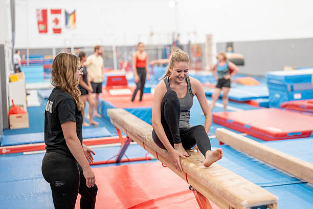 istock Young Women Practicing Gymnastics on Balance Beam with Instructor in Training Gym 2223265487