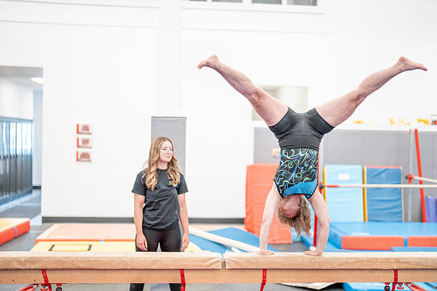 istock Gymnast Balancing on Beam with Supportive Trainer in Sport Hall 2223265510