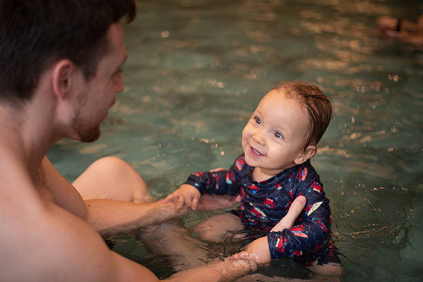 istock Baby in sunsuit romper looking at his dad in a pool 2223268964