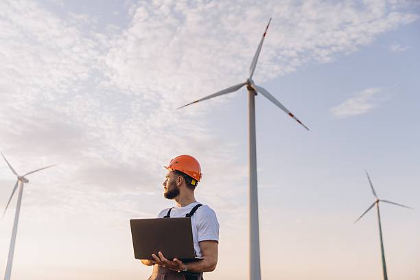 istock Engineer holding laptop inspecting wind turbines in a wind farm at sunset 2223273239