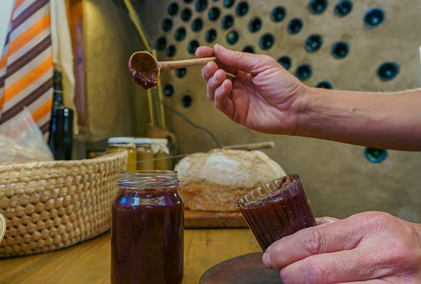 Hands holding a wooden spoon and a glass with fig jam, in a rustic kitchen