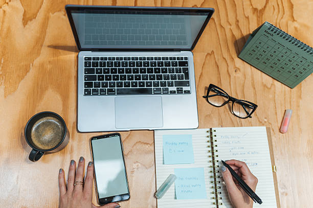 istock Overhead view of woman using digital devices, writing notes on notebook on desk 2223276577