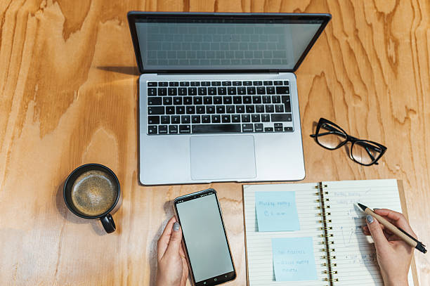 istock Overhead view of woman using digital devices, writing on notebook on desk 2223276588