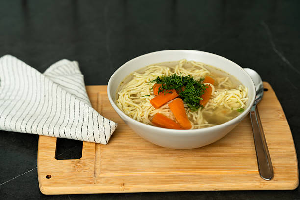 A close-up view of a bowl homemade chicken noodle soup, garnished with fresh dill and featuring vibrant carrot slices.