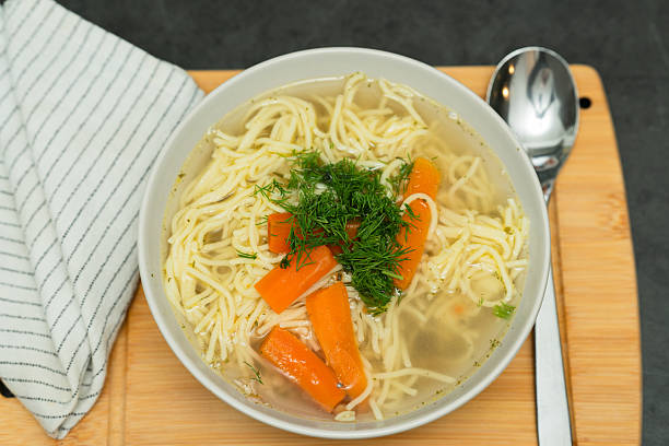 A close-up view of a bowl homemade chicken noodle soup, garnished with fresh dill and featuring vibrant carrot slices.