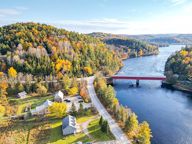 istock Small red bridge elegantly spanning a serene river in a vibrant autumn forest with colorful foliage 2223297560