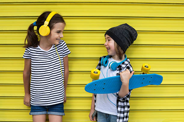 Happy boy and girl enjoying a fun day together, dressed in stripes and plaid, with headphones and a skateboard. Personality, character, independence, young spirit