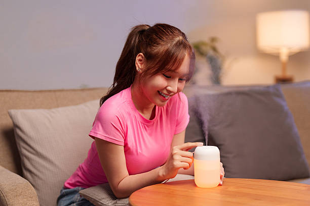 Adult Asian Woman Using Aromatherapy Diffuser for Relaxation & Longevity Lifestyle at Home with Essential Oils for a Calm and Peaceful Ambiance