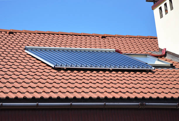 istock House rooftop solar water heating (SWH) is heating water by sunlight, using a solar thermal collector. House red clay tiles roof with solar water heating panel and attic skylights windows 2223318229