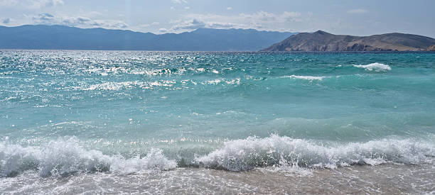 A view from Vela plaza in Baska of the turquoise sea with waves and Velebit and Prvic island in the distance