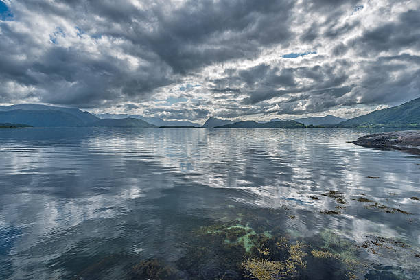 Majestic clouds cast shadows across tranquil waters, creating a stunning landscape at dusk in a beautiful coastal area.