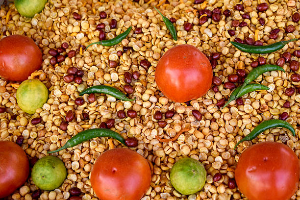 This image features a colorful mix of Indian snacks, including roasted chickpeas and peanuts, topped with fresh green chilies, juicy red tomatoes, and bright green lemons, hinting at their tangy and spicy flavors.
