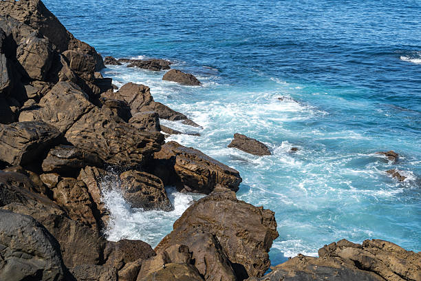Waves shimmer with turquoise light as they crash on ancient rocks, dancing in endless rhythm under the blue sky at the sea edge