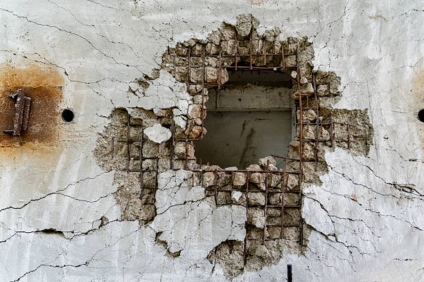A severely cracked and damaged concrete wall reveals exposed rebar and structural failure.