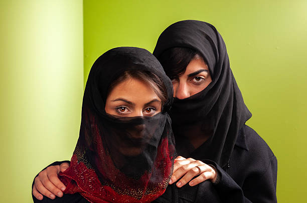 close up of two young Iranian women in veil looking at the camera against green background