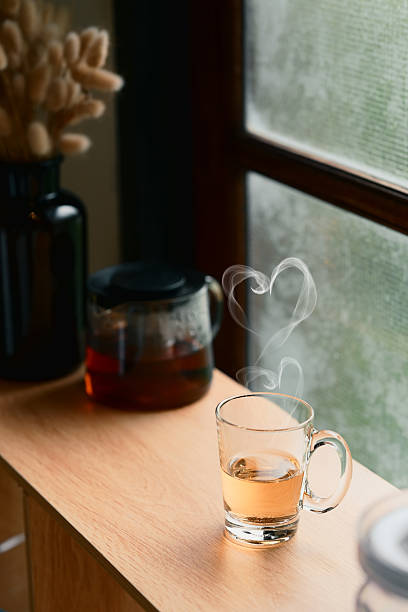 Glass cup of hot tea with heart shaped steam rising by the window, creating a warm and romantic atmosphere