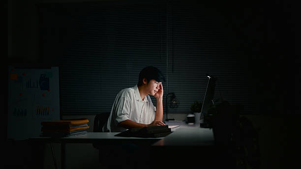 istock Tired office worker concentrating on his monitor while working alone in a dark office 2223341711