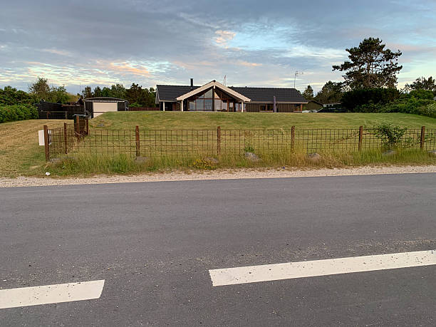 Scenic view of a countryside farmhouse encompassed by lush trees (possible genera: Populus, Salix, various broadleaves) and fields of green crops. The setting emphasizes rural tranquility and an idyllic natural landscape.