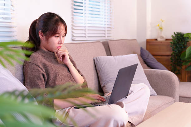 istock Asian woman thoughtfully using laptop computer on cozy living room couch embracing digital flexibility and modern connectivity at home 2223344853