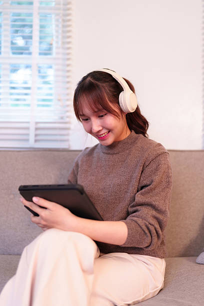 istock Young Asian Woman Connects with Artificial Intelligence through Tablet and Headphones for Enhanced Modern Daily Life 2223344879