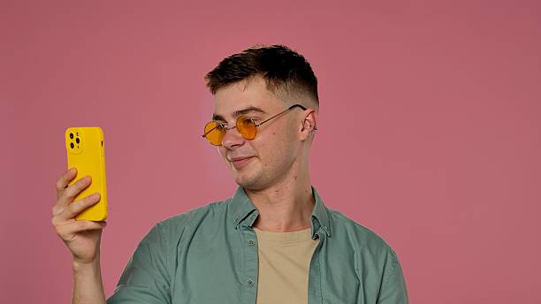 istock Man with Yellow Sunglasses and Smartphone in Pink Studio 2223350963
