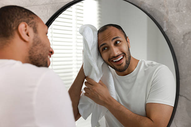 istock Smiling man with towel looking at mirror in bathroom 2223351204