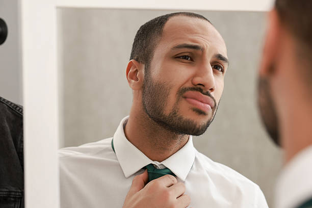 istock Handsome man adjusting necktie near mirror at home 2223351294
