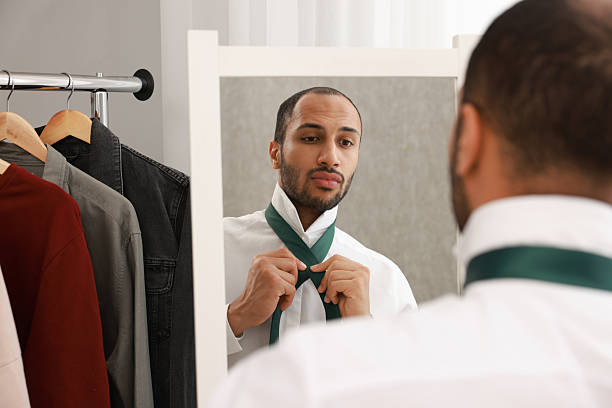 istock Handsome man adjusting necktie near mirror at home 2223351314