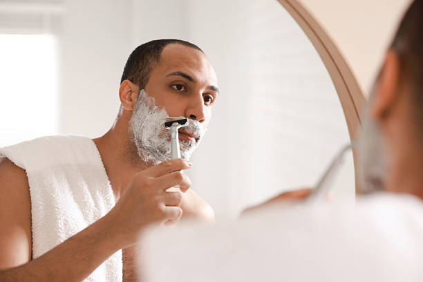 istock Handsome man shaving with razor near mirror in bathroom 2223351324
