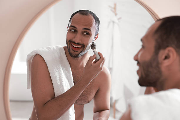 istock Smiling man applying shaving foam near mirror in bathroom 2223351418
