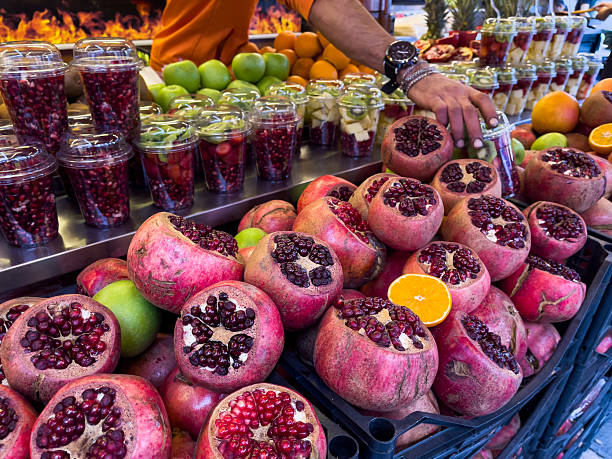 Street fruit stand in Istanbul displaying fresh pomegranates, oranges, apples, and ready-to-go fruit cups, with a vendor reaching for a cup under vibrant market lighting