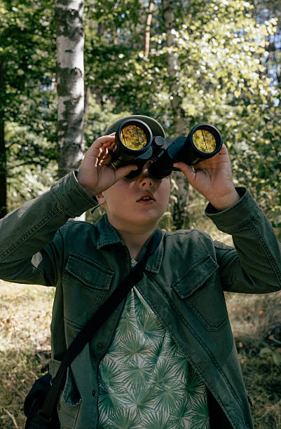 istock Boy backpacking in the green forest and tall grasses. Bird watching adventure. Looking through binoculars. Birding 2223355000