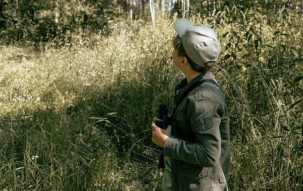 istock Boy backpacking in the forest and grasses. Bird watching adventure. Looking through binoculars. Birding 2223355014