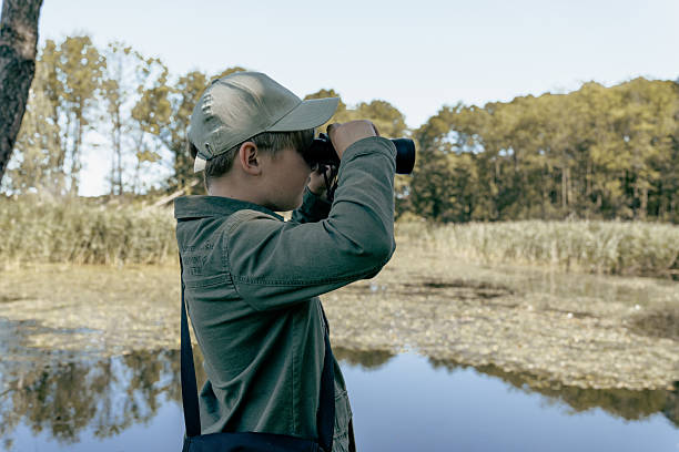 istock Boy backpacking in the summer forest by a lake. Bird watching adventure. Looking through binoculars. Birding 2223355038