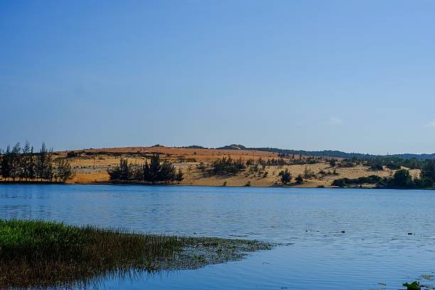 istock Serene sandy hill by a calm lake under a blue sky. 2223370512