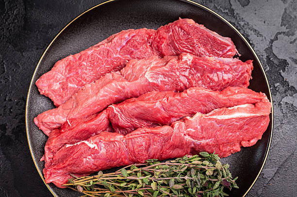 Raw sliced horse meat steaks presented with herbs and spices, inviting creativity in the kitchen for those seeking bold flavors and unique dining experiences. black background. top view