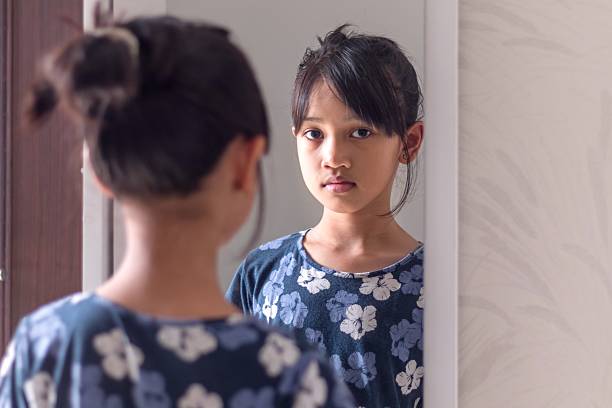istock A young Asian girl looking at herself in the mirror with a blank expression 2223373767