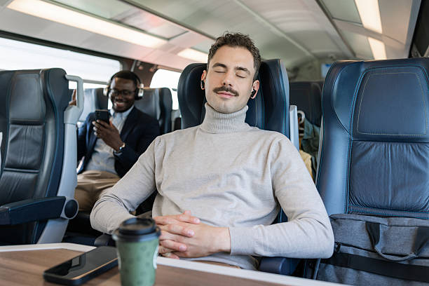 A man seated comfortably in a train enjoying audio through headphones, accompanied by warm coffee.