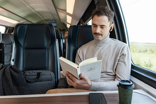 istock Man reading a book while traveling on a train with a scenic view 2223379351