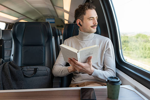 istock Man reading a book while traveling on a train with a scenic view 2223379386