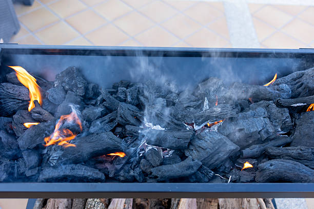 Charcoal igniting with visible flames and smoke rising in a grill, ready for outdoor cooking