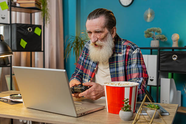 istock Excited happy senior man celebrating victory in play video game on laptop using controller joystick 2223391913