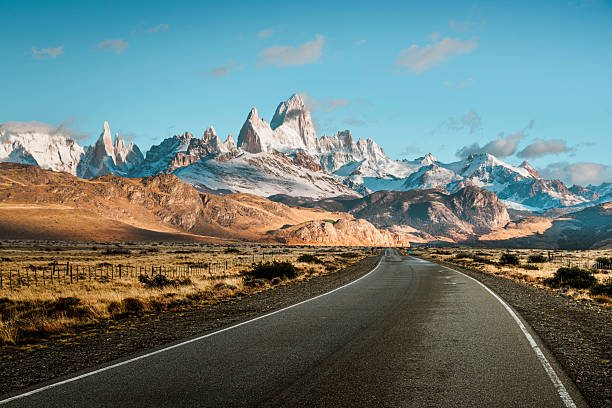 istock Open road leading to snow capped mountains under a bright blue sky 2223392554