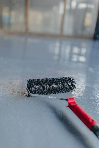 istock Worker applying resin on a gray industrial floor using a spiked roller 2223401122