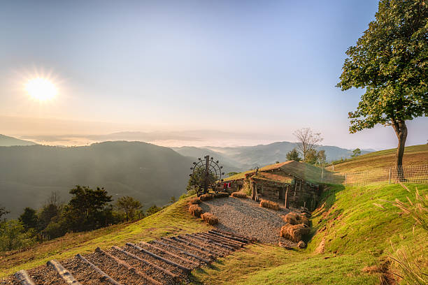 A breathtaking view of a sunrise over majestic mountains, featuring a rustic cabin on a grassy hillside. Ideal for conveying tranquility and nature's beauty.