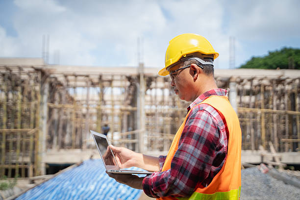 istock Asian male engineer supervising construction work checking blueprint on laptop at construction site 2223405393